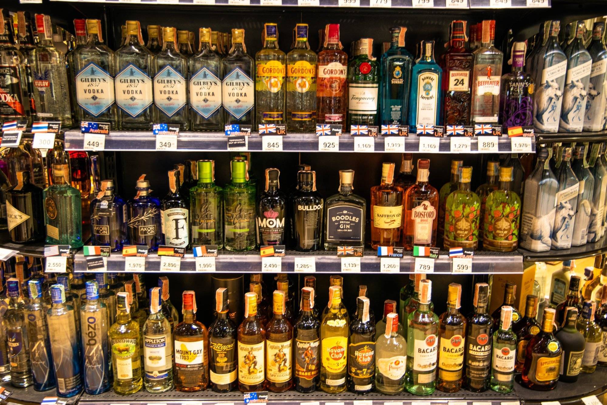 Assortment of liquor including gin, vodka, rum, whisky, etc. on the shelves with price tag in a supermarket.